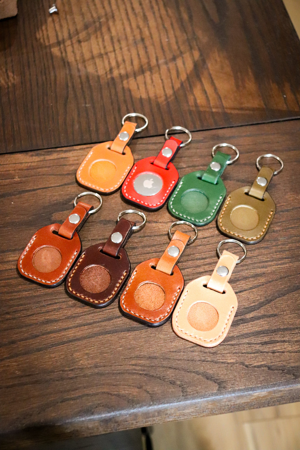 A collection of hand-stitched leather keychains in various colors including black, brown, red, green, and yellow, designed to hold AirTags.